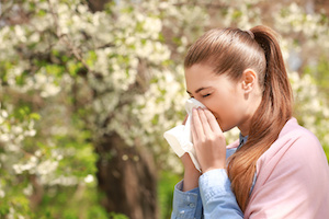Ung kvinna i en blomstrande park som nyser på grund av med pollen allergi